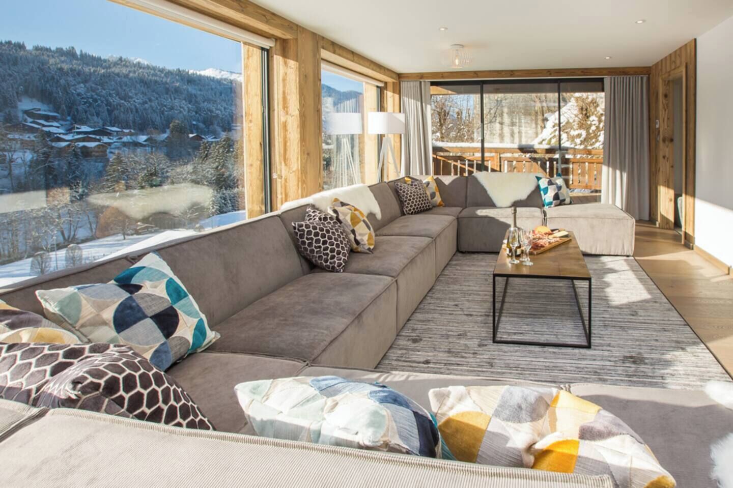 En moderne stue med en stor modulsofa, et sofabord og udsigt til et snelandskab gennem store vinduer.