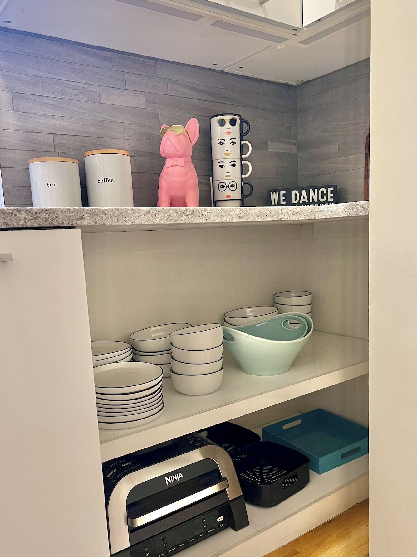 A kitchen with white cabinets, a coffee machine, a tea canister, and a 'We Dance' sign.