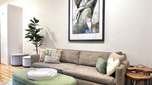 Un salon avec un canapé gris, un pouf vert, une petite table en bois et un tableau abstrait encadré accroché au mur.