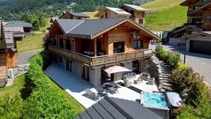 A chalet-style building with a balcony, outdoor seating, and a hot tub. - Chalet Le Pre hosted by More Mountain Morzine | Luxury 6 Bed 6 Bath Chalet | Sleeps 14. Only 10 min walk into the heart of Morzine with huge outdoor Jacuzzi, large terrace & garden with stunning views of the slopes. Secluded position, yet central. (Morzine)