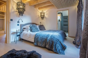 Een slaapkamer met een groot bed, een nachtkastje, een stoel en twee hanglampen.