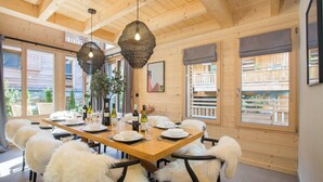 A wooden dining room with a large table set for six, surrounded by fluffy white chairs. - Chalet Verjus hosted by More Mountain, Morzine | Luxury 5 Bed 5 Bath Chalet | Sleeps 10. Luxury stand alone ski chalet in a very central location with Outdoor Jacuzzi & large terrace. All Mod Cons. Less than 5 mins walk to Ski Lifts. (Morzine)