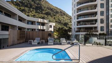 A rooftop pool with lounge chairs, a wooden deck, and a mountainous backdrop.