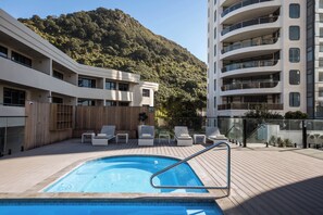 Ein Pool auf dem Dach mit Liegestühlen, einer Holzterrasse und einer Bergkulisse.