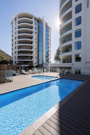 A modern hotel with a pool, multiple balconies, and a clear sky. - Sunrise to Sunset Ocean Harbour Views Pool Spa Gym (Mount Maunganui)