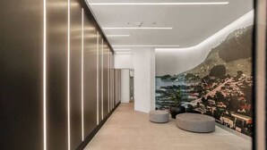 A modern hallway with a mural of a mountainous landscape, recessed lighting, and a seating area with ottomans.