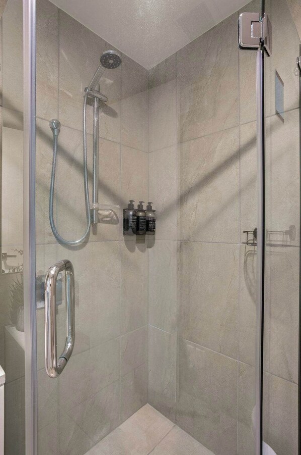 A glass-enclosed shower with a handheld showerhead and a wall-mounted faucet.