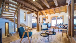 Un amplio salón con techo de madera, una escalera, un comedor y una cocina visible a través de una puerta abierta.