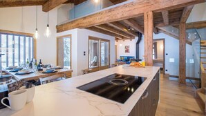 Una cocina moderna con encimera de mármol, vigas de madera e iluminación colgante.