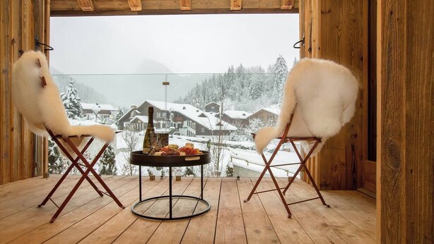 Una terraza de madera con dos sillones de pelo que dan a una vista nevada de la montaña.