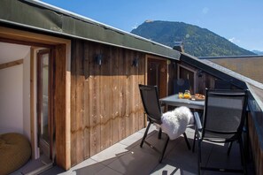 En træterrasse med et bord og stole, et luftigt hvidt objekt, og et bjerglandskab i baggrunden.