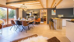 A modern interior with a dining area, kitchen, and a view through a large window. - Apartment Grand Central hosted by More Mountain, Morzine | Luxury 3 Bed 3 Bath | Sleeps 6. Luxurious and Spacious duplex Penthouse apartment in the centre of Morzine, only 2 minutes walk on the flat to both the Pleney and Super Morzine Telecabines. (Morzine)