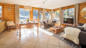 Tilava olohuone, jossa on puusisustus, ruokailutila kahdelle katetulla pöydällä sekä suuri ikkuna, josta avautuu näkymä ulos.