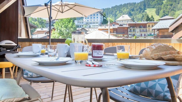 A breakfast table set outdoors with a view of a mountain town. - Apartment La Poste hosted by More Mountain, Morzine | Large 3 Bed 2 Bath apartment | Sleeps 6 . Fantastic location with  large terrace in the centre of town. Family friendly with All Mod Cons. Only 5 mins walk to Ski Lifts and (Morzine)