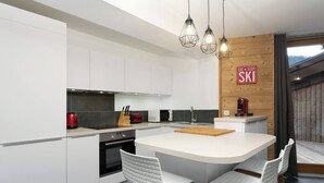 A modern kitchen with white cabinetry, a central island with stools, and a wooden accent wall with a 'Ski' sign. - Apartment La Poste hosted by More Mountain, Morzine | Large 3 Bed 2 Bath apartment | Sleeps 6 . Fantastic location with  large terrace in the centre of town. Family friendly with All Mod Cons. Only 5 mins walk to Ski Lifts and (Morzine)