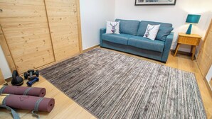 Ein Zimmer mit einem blauen Sofa, einem Holzschrank, einem gemusterten Teppich und Trainingsgeräten.
