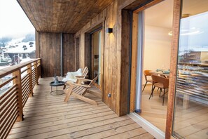 Eine Holzdielen-Terrasse mit Glastür zu einem Essbereich, ausgestattet mit Stühlen und einem Tisch.
