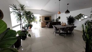 Een ruime zithoek met een grote eettafel, verschillende potplanten en een comfortabele zithoek.