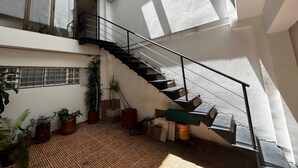 Ruime binnenzone met een trap naar een hoger gelegen verdieping, omringd door potplanten en verschillende objecten op de vloer.