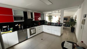 Een moderne keuken met witte en rode kastjes, een ingebouwde magnetron, en een eethoek met een zwarte stoel en tafel.
