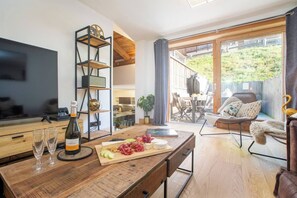 Eine moderne Küche mit Holzausziehtisch, Weingläsern und einer Weinflasche. Ein Essbereich mit Tisch und Stühlen bietet einen Blick ins Freie durch große Fenster.