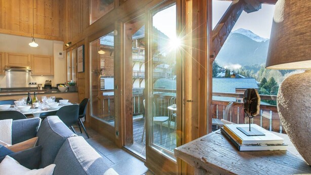 A cozy wooden interior with a dining area, large windows, and a view of mountains.