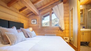 A wooden cabin bedroom with a large bed, a window with curtains, and a view of the outdoors.