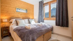 Een knus slaapkamer met een houten hoofdbord, een bed met meerdere kussens, een nachtkastje met een lamp en een raam met gordijnen.