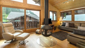 Ein gemütliches Blockhaus-Interieur mit einem großen Kamin, Ledersitzmöbeln und großen Fenstern mit Blick auf den umliegenden Wald.