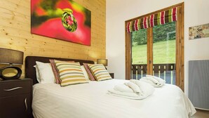 Ein ordentlich gemachtes Bett mit weißen Leinentüchern und gestreiften Kissen, ein hölzerner Kopfteil und ein Fenster mit Blick auf Grünflächen.