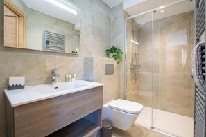 Une salle de bain moderne avec un lavabo blanc, un meuble-lavabo en bois, une cabine de douche en verre et des toilettes.