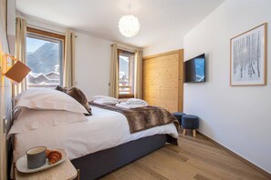 Une chambre d’hôtel moderne dotée d’un grand lit, d’un parquet, d’un téléviseur fixé au mur et offrant une vue sur la montagne.