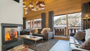 A cozy living room with a fireplace, sofas, and a view of a snowy mountain landscape. - The Crows Nest hosted by More Mountain, Morzine | Luxury 5 Bed 5 Bath Private Chalet | Sleeps 10.  Fantastic Central location in Morzine in the heart of the village. Family friendly with All Mod Cons. Only 5 mins walk to Ski Lifts. (Morzine)