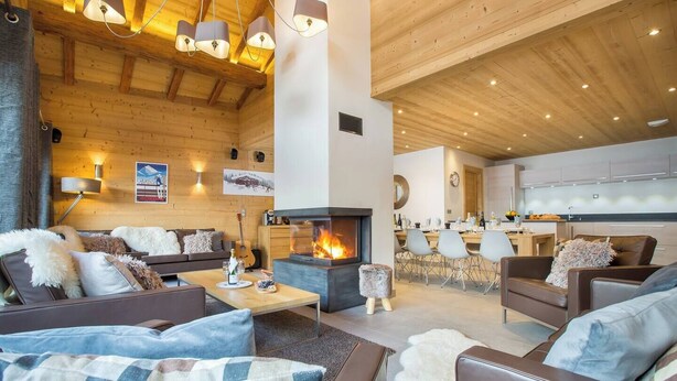 A cozy living room with a fireplace, wooden ceiling, and modern furniture. - The Crows Nest hosted by More Mountain, Morzine | Luxury 5 Bed 5 Bath Private Chalet | Sleeps 10.  Fantastic Central location in Morzine in the heart of the village. Family friendly with All Mod Cons. Only 5 mins walk to Ski Lifts. (Morzine)