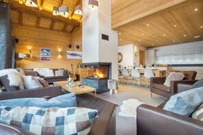 Een gezellige woonkamer met een open haard, houten plafond en moderne meubels.