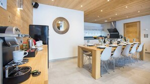 A modern kitchen with a coffee machine, a refrigerator, and a dining area with a wooden table and chairs. - The Crows Nest hosted by More Mountain, Morzine | Luxury 5 Bed 5 Bath Private Chalet | Sleeps 10.  Fantastic Central location in Morzine in the heart of the village. Family friendly with All Mod Cons. Only 5 mins walk to Ski Lifts. (Morzine)