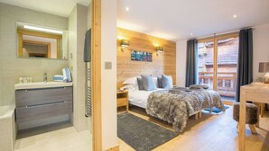 A modern bedroom with a wooden headboard, a large bed with a furry throw, a nightstand, and a wooden desk with a chair. - The Crows Nest hosted by More Mountain, Morzine | Luxury 5 Bed 5 Bath Private Chalet | Sleeps 10.  Fantastic Central location in Morzine in the heart of the village. Family friendly with All Mod Cons. Only 5 mins walk to Ski Lifts. (Morzine)
