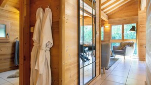 Ein Holzblockbau-Innenraum mit Glastür zu einem Essbereich, einem Sofa und einem Sessel.