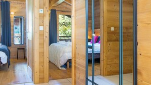 Eine Holzhütte mit einem Schlafzimmer, das ein Bett, einen kleinen Tisch und ein Fenster mit Vorhängen bietet.