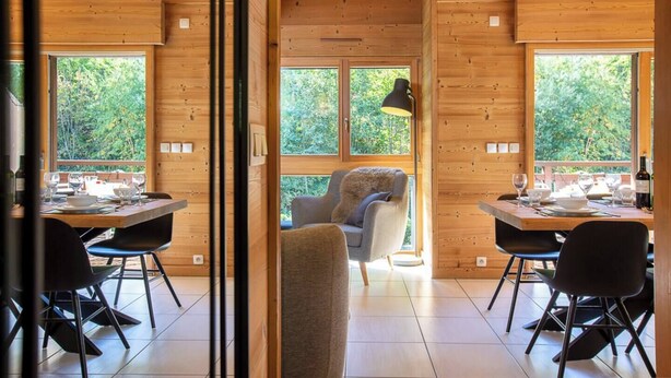 Eine Holzhütte mit zwei Esstischen, Stühlen und einem Sofa.