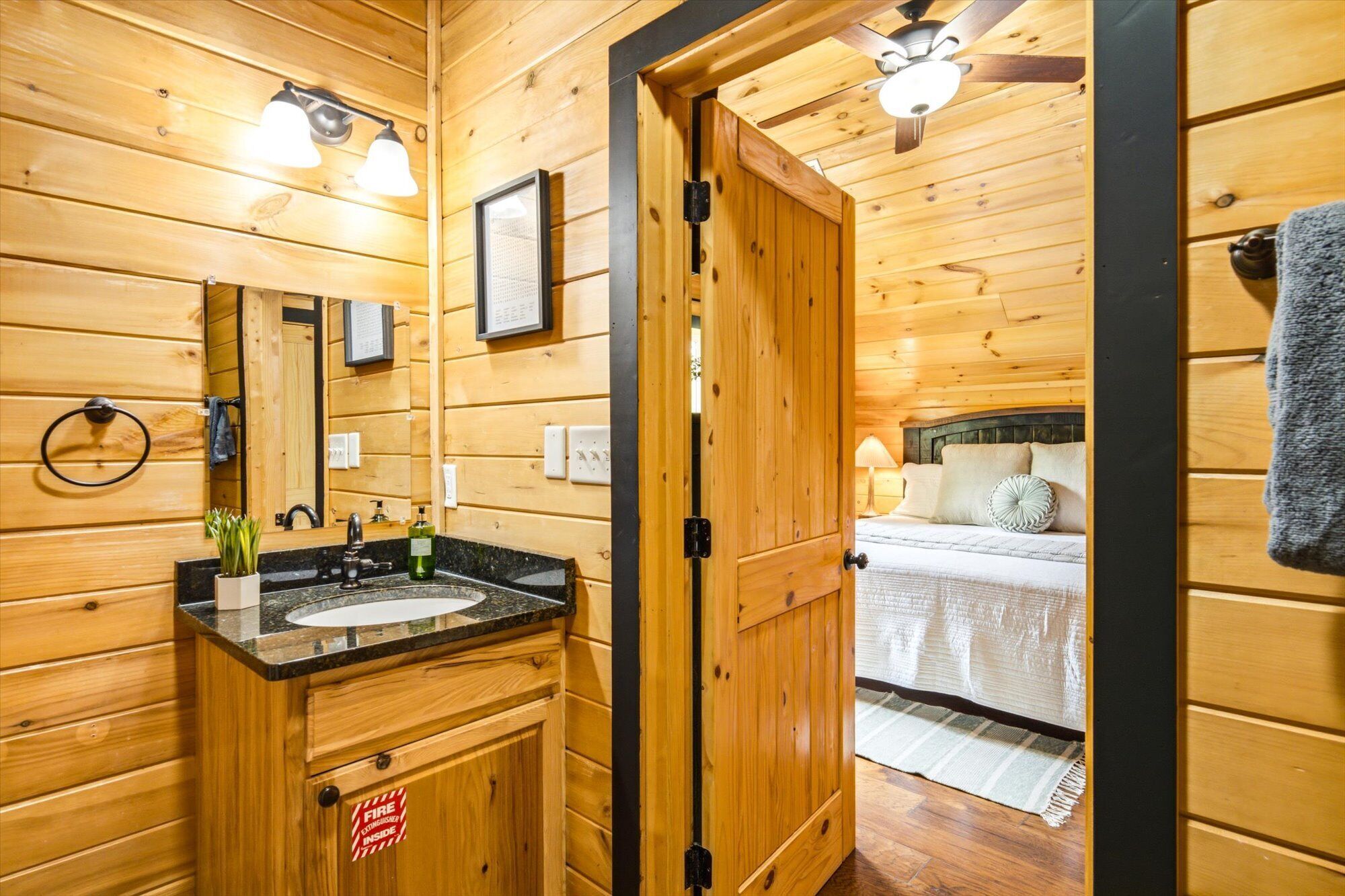 A wooden cabin interior with a bathroom featuring a sink, mirror, and towel ring.