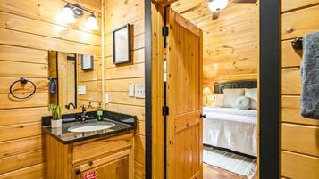 A wooden cabin interior with a bathroom featuring a sink, mirror, and towel ring.