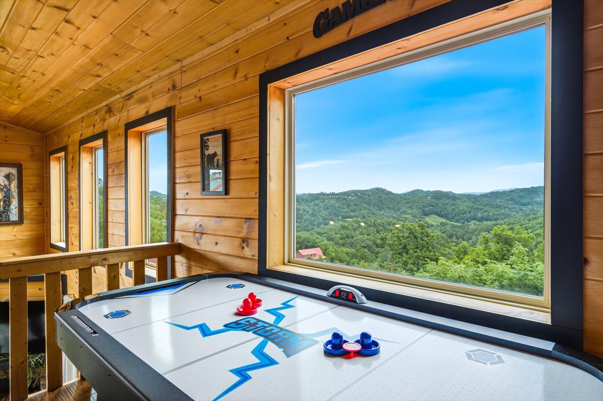 Une pièce en bois avec une table de jeu de «shuffleboard», de grandes fenêtres et une vue sur une montagne boisée.