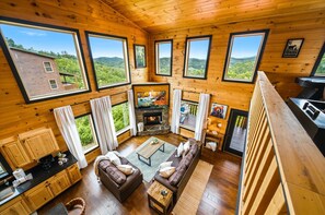 A cabin with large windows, a fireplace, a sofa, and a dining area. - Heavenly Daze (Sevierville)