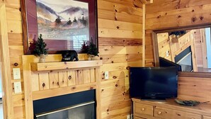 A wooden cabin interior with a fireplace, a television, and a small Christmas tree.