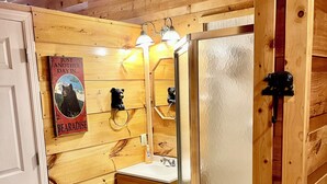 A wooden cabin bathroom with a wooden vanity, a glass shower enclosure, and a ceiling fan.