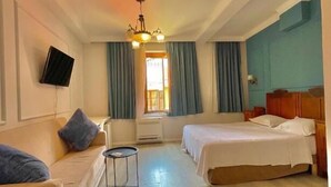 A hotel room with a sofa, two single beds, a small table, and a TV mounted on the wall. - Hotel Promenade (Shkodër)