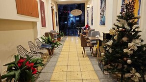 A hotel lobby with a tiled floor, seating area with chairs and tables, a Christmas tree, and a sign for Promenade Hotel. - Hotel Promenade (Shkodër)
