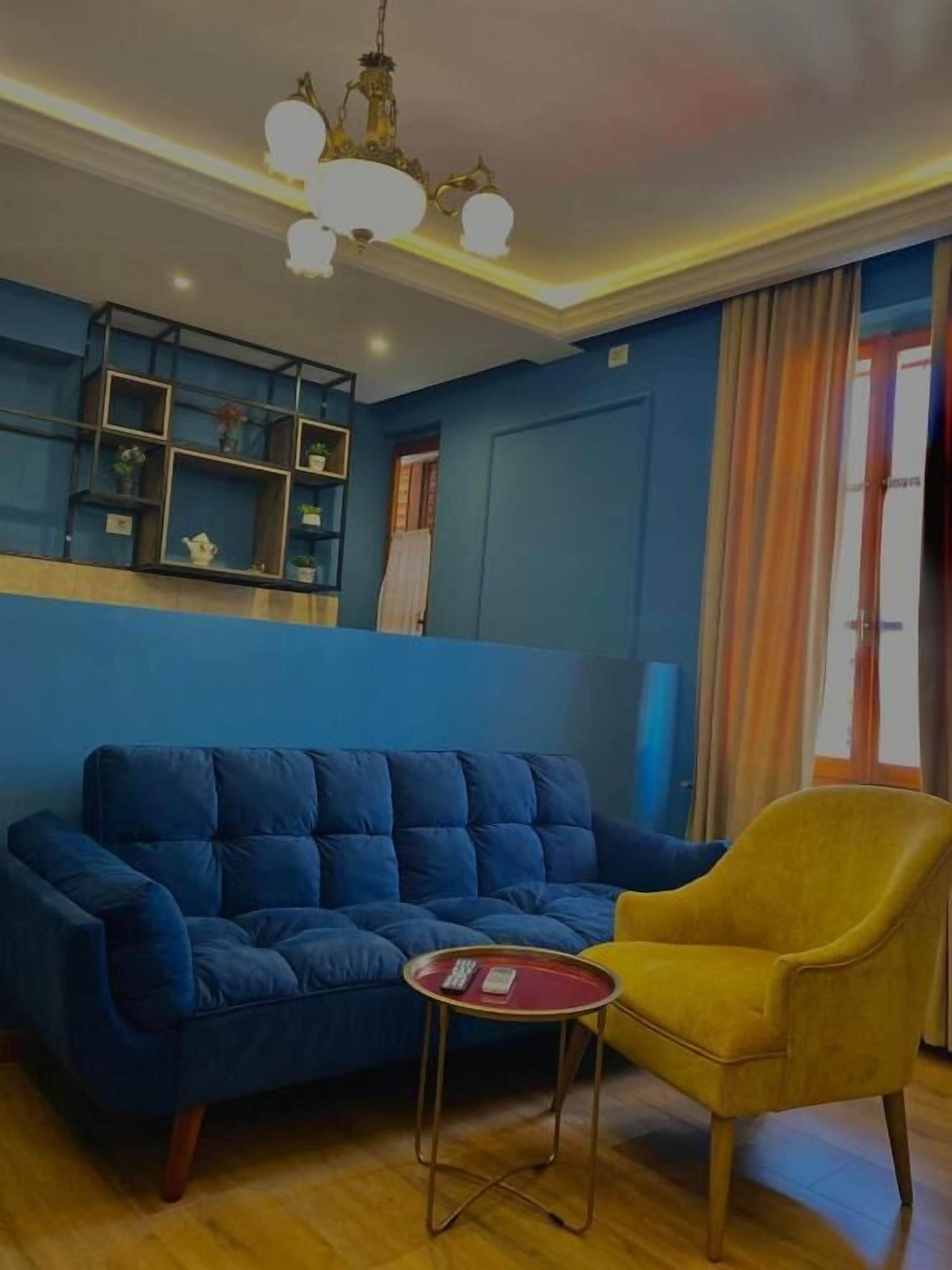 A room with a blue sofa, a yellow armchair, a small round table, and a ceiling light fixture.