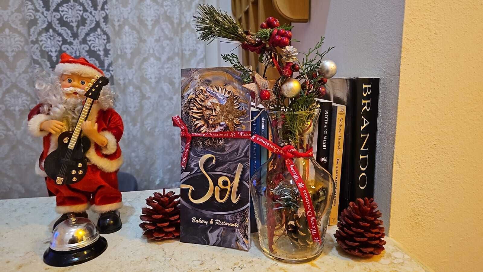 A Santa figurine holding a guitar, a decorative glass bottle with a Christmas ribbon, and a book titled 'Sol'.